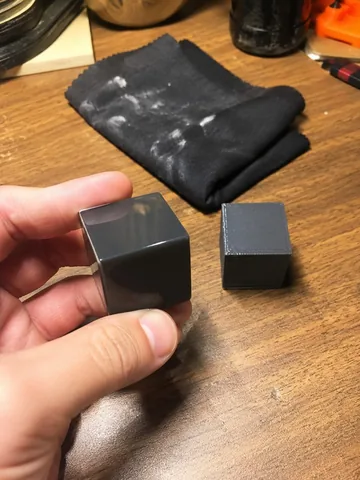A finished dark cube held next to a raw layer-lined cube on the desk