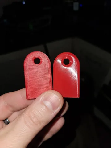 Two red printed parts held in hand: raw layer lines on the left, smooth gloss on the right