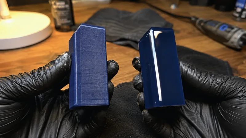 Two dark-blue printed blocks held in gloved hands: raw layer lines on the left, a glossy finished surface on the right